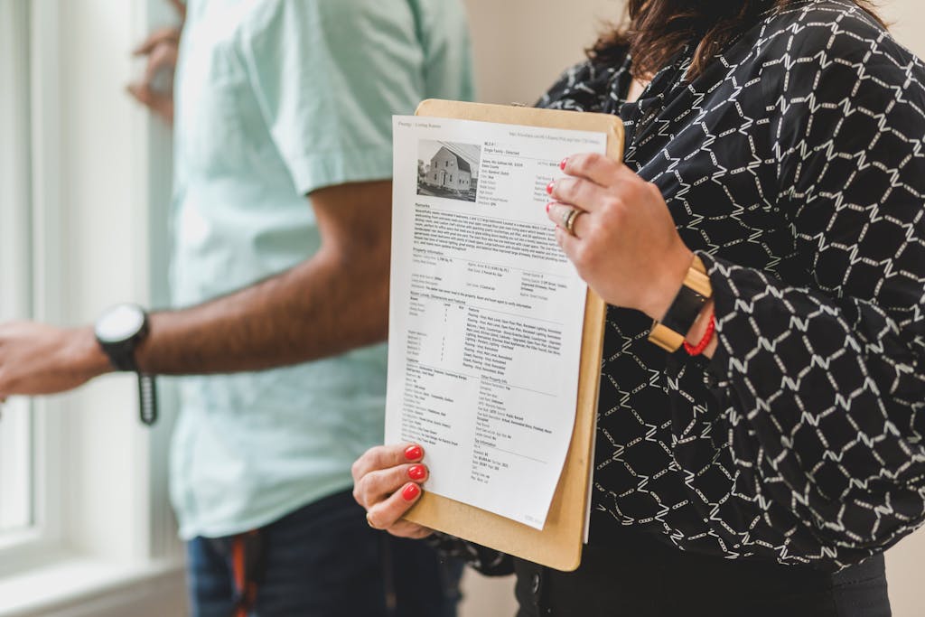 Real estate agent holding property documents on a clipboard in an office setting.